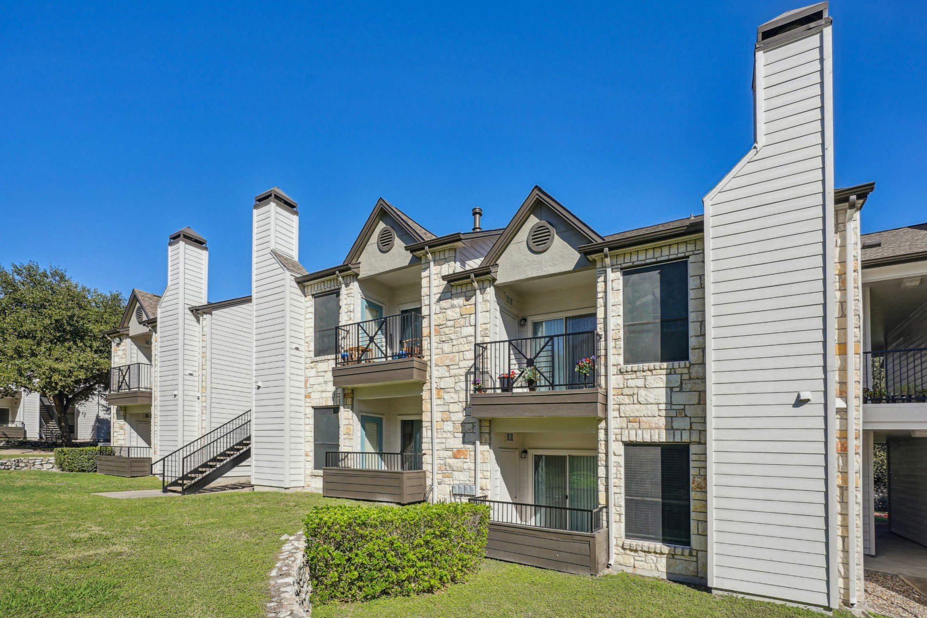 Row of our apartment buildings with balconies and a clear blue sky at On the Green apartments in Austin, TX